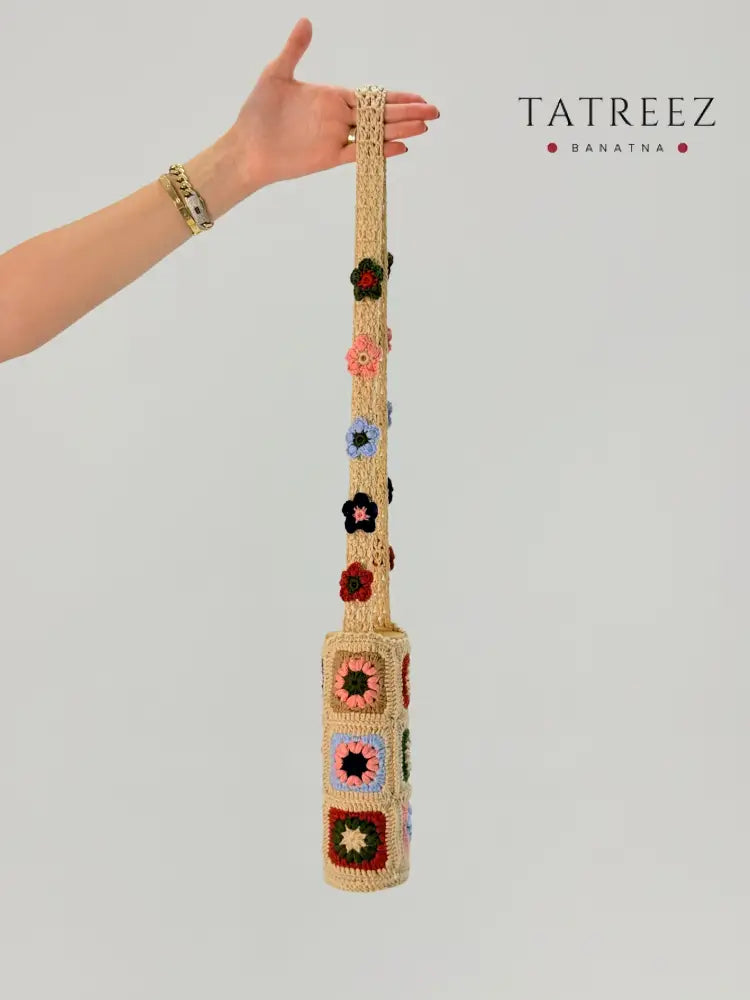 Hand-crocheted bottle cover in floral granny square pattern with beige, pink, blue, and multicolor details, made by Palestinian and Jordanian women artisans seeking financial independence while preserving regional craft heritage.