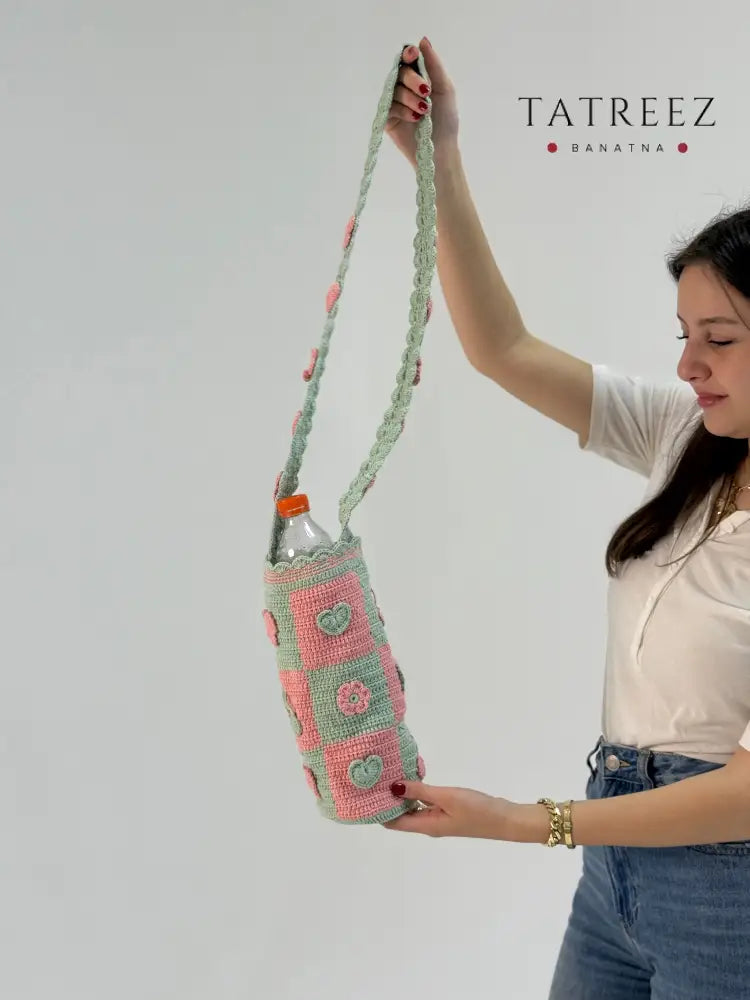 Handmade light teal and peach crochet bottle cover with geometric block design, crafted by Palestinian and Jordanian women artisans, eco-friendly reusable bottle holder.