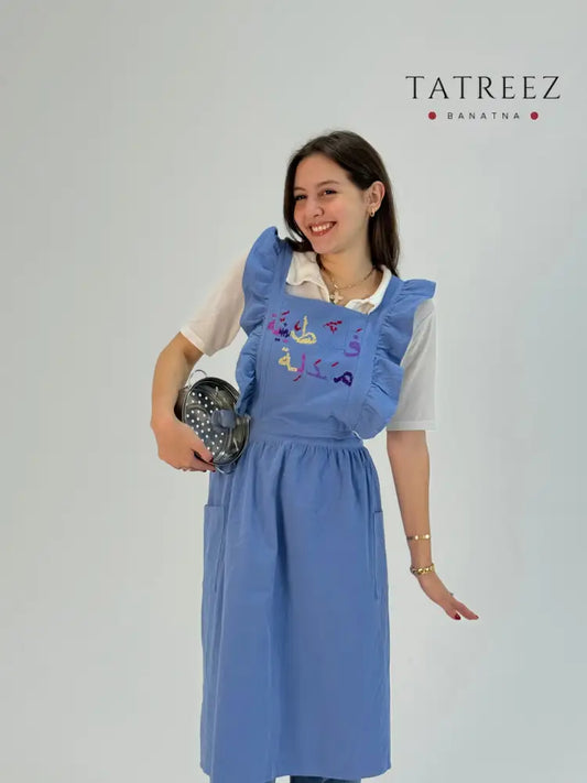 Handmade blue waterproof apron with Falasteeniya Maadale Palestinian embroidery, crafted by women artisans.