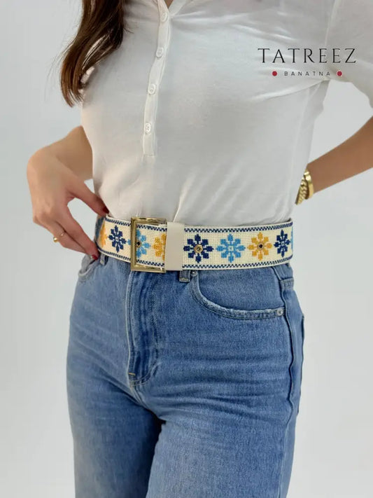 Handmade adjustable belt with floral tatreez embroidery in blue and yellow on cream, worn with jeans
