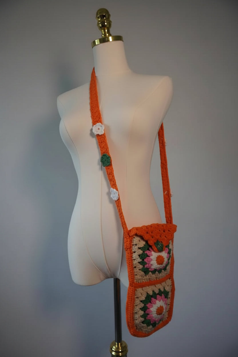 Handmade crochet phone case featuring a vibrant design of flower granny squares in shades of orange, pink, white, and beige. The case is designed for everyday use and includes a long strap for easy carrying.