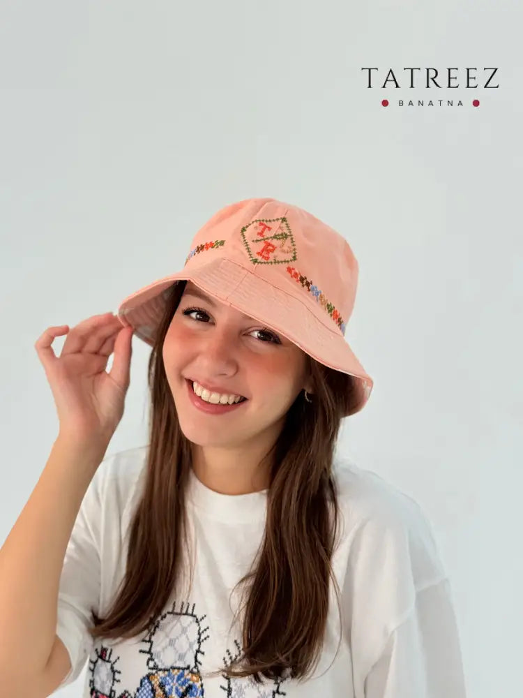Handmade peach bucket hat with TB logo and simple tatreez embroidery.