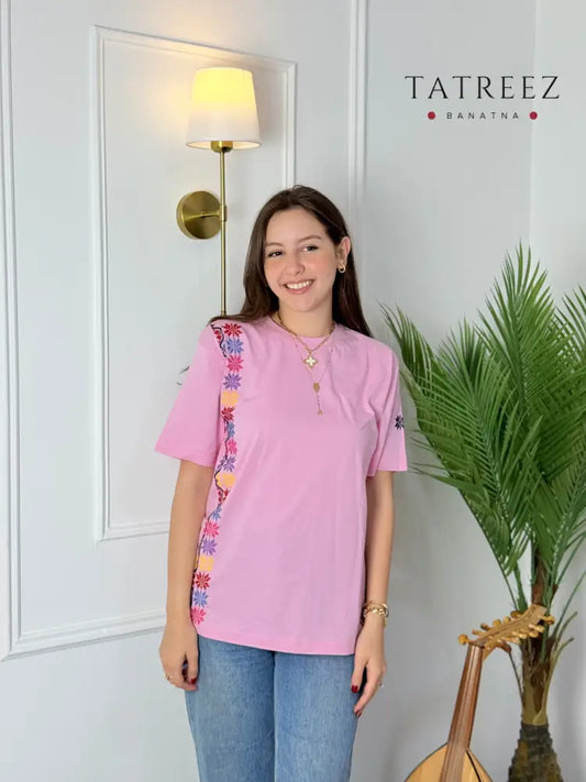 Light pink cotton t-shirt with Palestinian tatreez embroidery on the sleeve and side, modeled with jeans, handmade by women artisans