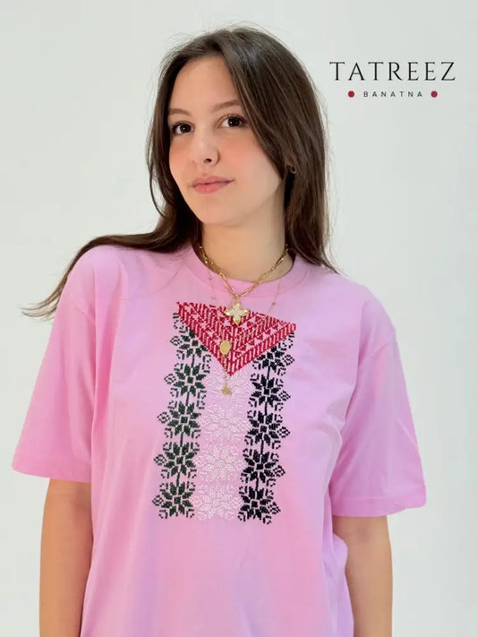Pink cotton t-shirt featuring hand-embroidered Palestinian flag colors in traditional tatreez pattern, youth cultural heritage wear