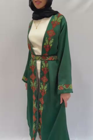 Handmade green abaya robe with embroidered Palestinian motifs and a belt, made from Kadeena fabric. The robe has a shoulder length of 45 cm and an overall length of 128 cm. Model is 173 cm tall wearing a small/medium size, showcasing the robe's elegance.