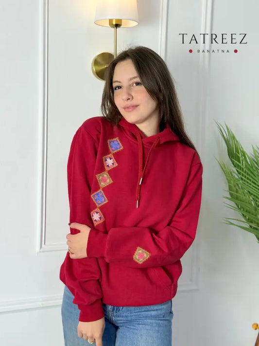 Red cotton hoodie with colorful hand-stitched Palestinian tatreez embroidery along the side and sleeve, modeled by a woman, handmade by women artisans
