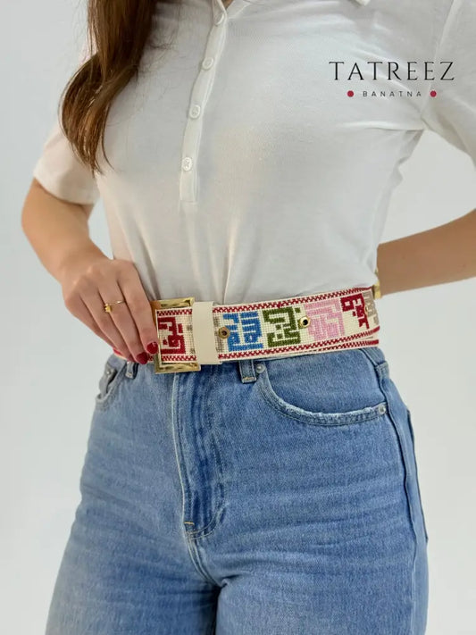 Handmade adjustable belt with Palestinian city names in colorful tatreez embroidery on cream fabric
