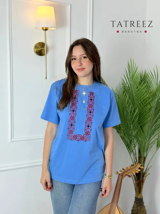 Cotton t-shirts in light blue and pink with U-shaped Palestinian tatreez embroidery, modeled with jeans, handmade by women artisans